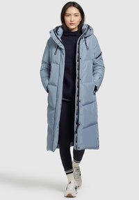Piumino blu chiaro con cappuccio, chiusura frontale a zip e bottoni a pressione; presenta tasche laterali e un marchio discreto sulla zip.