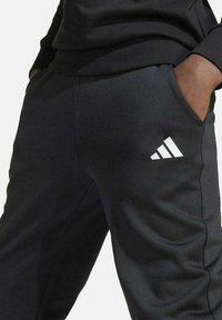 Zwarte sportbroek van zachte stof, met een slim fit, elastische tailleband, zijzakken en een witte logo-detail met drie strepen.