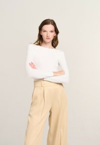 White long-sleeve top with a boat neckline, paired with high-waisted beige pleated trousers. Smooth fabric and fitted design.