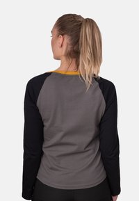Graues Langarmshirt mit schwarzen Ärmeln und gelben Kragenakzenten. Glatte Textur, figurbetontes Design und abgerundeter Saum unten.