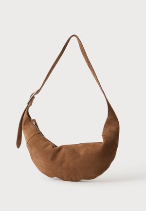 Sac d’épaule en daim marron en forme de croissant avec bandoulière réglable et fermeture éclair supérieure sur un fond clair uni.