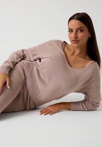 Conjunto de loungewear de color rosa claro, que incluye un suéter suelto y con los hombros al aire, y pantalones ajustados con puños acanalados y una cinturilla elástica.