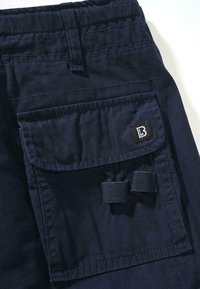 Granatowe spodnie cargo wykonane z wytrzymałej tkaniny, z dużą przednią kieszenią na klapę, przeszyciami i małą metką z logo.