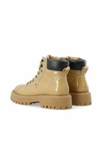Bottines en cuir verni beige avec des accents noirs, présentant un bout rond, une semelle extérieure en caoutchouc épaisse et des œillets filetés.