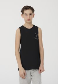 Maglietta nera senza maniche con scollatura tonda e piccolo logo bianco "LA" sul lato sinistro del petto, abbinata a pantaloni della tuta grigi chiari.