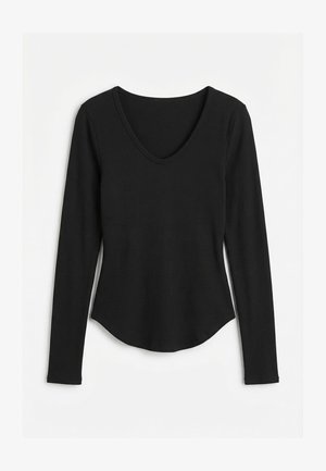 Sort langærmet ribstrikket top med scoop-halsudskæring og buet kant, lagt fladt på en hvid baggrund.