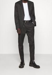 Randig kostym i mörkgrå och svart tyg, åtsittande design, en knapp, kombinerad med en vit T-shirt och svarta läderstövlar.