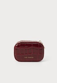Pequeña funda rectangular con textura de cocodrilo en color burdeos, con el logotipo dorado de Ted Baker y un tirador de cremallera, sobre un fondo blanco.