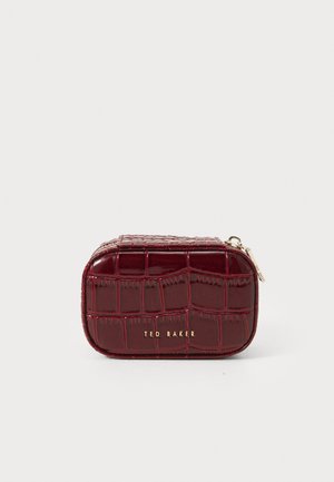 Klein rechthoekig maroon leren etui met krokodillenstructuur, voorzien van een gouden Ted Baker-logo en ritssluiting, op een witte achtergrond.