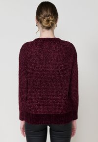 Gestrickter burgunderfarbener Pullover mit strukturiertem Finish, Rippbündchen und Saum. Verfügt über einen runden Halsausschnitt und eine lockere Passform. Rückenansicht gezeigt.