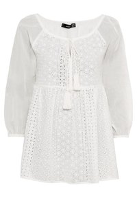 White dress with a textured, embroidered bodice featuring hexagonal cut-outs, a tie detail at the neckline, and sheer long sleeves.