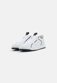 Sneaker bianche con accenti neri, parte superiore in pelle morbida, punta perforata, chiusura con lacci e logo GUESS di lato. Suola in gomma.