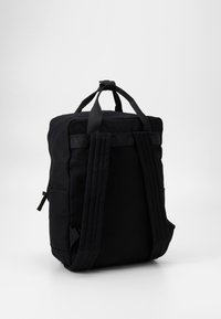 Sac à dos en toile noire avec des bretelles rembourrées, une poignée supérieure et une poche latérale, au design rectangulaire et minimaliste.