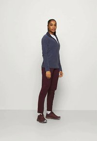 Navy zip-up fleece jacket, fitted, paired with maroon tapered pants and dark sneakers. Smooth texture, simple design, no visible patterns.
