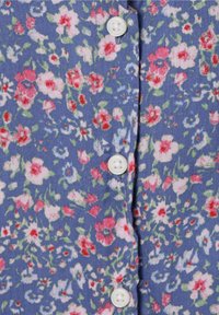 Blauer Stoff mit kleinem pinkfarbenem, weißem und rotem Blumenmuster und weißen Knöpfen in der Mitte.