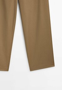 Pantalon marron à jambes droites avec coutures latérales visibles et texture de tissu lisse sur fond blanc.
