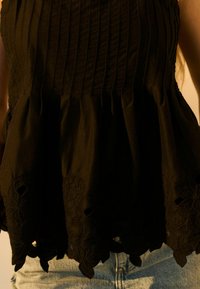 Haut peplum noir en tissu texturé avec des rayures verticales et broderie florale sur l'ourlet, mettant en valeur des motifs découpés complexes.