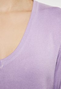 Lavenderfarbener V-Ausschnitt-Pullover mit weicher Textur, der gerippte Kanten und ein leichtes Strickdesign aufweist, mit Fokus auf dem Hals- und Schulterbereich.