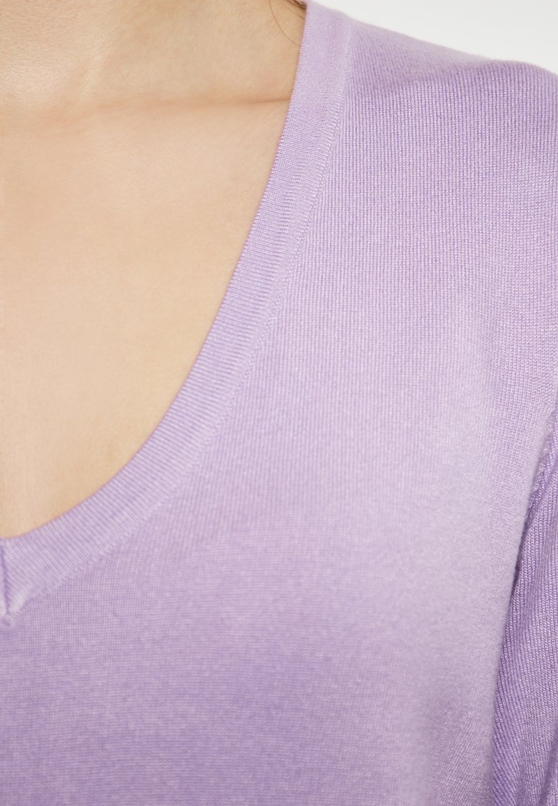 Lavenderfarbener V-Ausschnitt-Pullover mit weicher Textur, der gerippte Kanten und ein leichtes Strickdesign aufweist, mit Fokus auf dem Hals- und Schulterbereich.