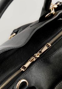 Close-up van een zwarte leren handtas met een gouden rits en hardware, die het strakke ontwerp en de gladde textuur benadrukt.