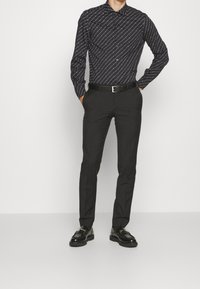 Czarna koszula z długim rękawem z białymi ukośnymi liniami, zestawiona z dopasowanymi czarnymi spodniami i błyszczącymi czarnymi butami, z cienkim czarnym paskiem.