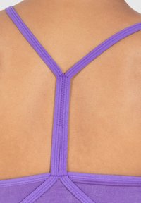 Violetti urheilu-toppi, jossa on ohuet hihnat, Y-taustasuunnittelu ja sileä pinta vaaleanruskeaa taustaa vasten.