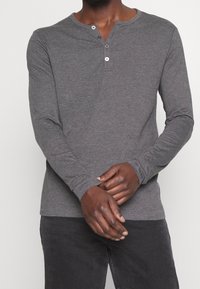 Grijze langesleeve Henley-shirt met een drie-knopen sluiting. Zachte textuur en slim fit, gecombineerd met donkergrijze broeken.