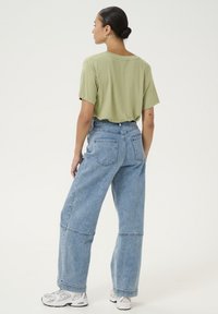 T-shirt din bumbac verde deschis, cu un croi lejer și mâneci scurte, combinat cu blugi din denim albastru deschis, cu talie înaltă și croi larg.