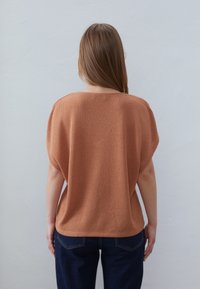 Krátký rukáv, volný top v měděné pletenině se strukturou. Pairs s tmavě modrými džíny.