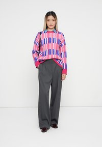 Multicolored knit sweater with pink, purple, and blue patterns, paired with gray wide-leg trousers and shiny burgundy shoes.