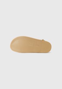 Suola di una scarpa caratterizzata da una superficie liscia in gomma beige chiaro, con motivi sottili e un logo centrale in rilievo. Design piatto, bordi arrotondati.