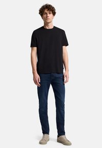 Svart kortärmad t-shirt, rund hals, matchad med mörkblå jeans och beige sneakers. Rak passform, slät yta, minimalistisk design.