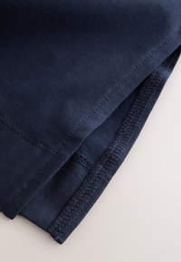 Détail de tissu bleu marine avec une texture lisse, présentant des coutures renforcées le long des ourlets et une couture plate pour la durabilité.