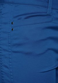 Blue fabric of pants with a smooth texture, featuring a flat front pocket with two small black buttons for detail.