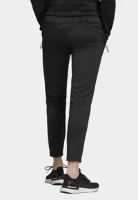 Schwarze Sweatpants aus einem weichen Stoff, mit schmaler Passform, Kordelzugbund und Seitentaschen, kombiniert mit schwarzen Sportschuhen.