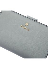 Hellgraue Lederbörse mit genarbter Textur, ausgestattet mit einem goldenen Markenlogo "FURLA" und einem sicheren Druckverschluss. Elegante Nahtdetails.