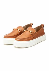 Zapatos de charol color miel, tipo slip-on, con suela blanca gruesa, presentan un detalle decorativo de eslabones dorados en la parte delantera y un borde cosido.