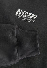 Černá mikina s vroubkovanými manžetami, jemnou texturou a bílým potiskem s textem "20 STUDIO W. COAST DEPT." včetně podrobností o lokalitě.