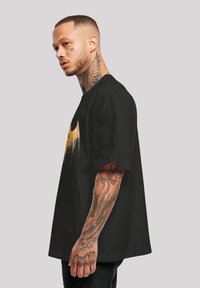 Melnā lielā T-kreklā ar zelta grafisko dizainu. Audums šķiet gluds, ar īsām piedurknēm un brīvi pieguļošu piegriezumu.