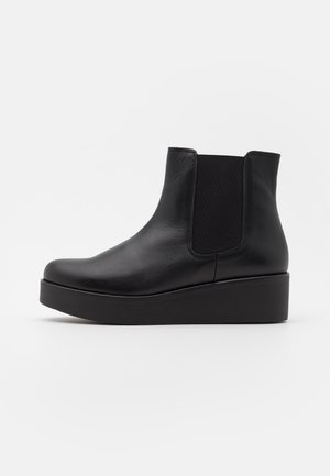Bottine noire en cuir avec panneau latéral élastique et semelle épaisse à plateforme, vue de profil sur fond blanc.