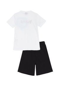 Maglietta in cotone bianco con grafica grigia sbiadita sul retro, abbinata a pantaloni corti in cotone neri con vita elasticizzata.