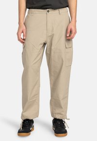 Beige cargo bukser med en afslappet pasform, der har sidelommer, en snøre i kanten og et let, struktureret stof.