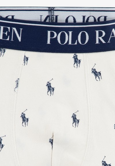 Bijeli bokserice s tamnoplavim elastičnim pojasom. Sadrži ponavljajući uzorak logotipa s tamnoplavim igračem polo, s glatkom teksturom tkanine.
