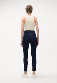Λεπτά τζιν σε σκούρο μπλε τ denim με ψηλή μέση, διαθέτοντας πίσω τσέπες και στενά πόδια. Συνδυασμένα με ένα ανοιχτόχρωμο μπλουζάκι και λευκά αθλητικά παπούτσια.
