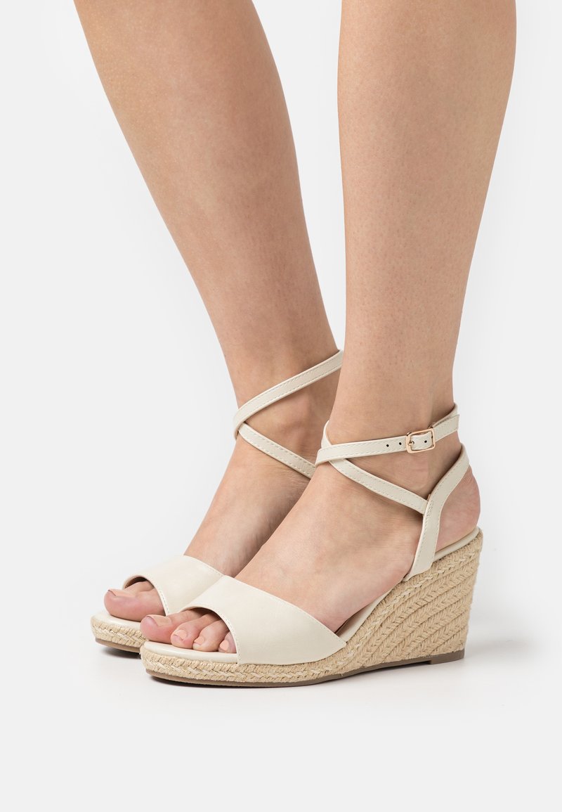 Beige kile sandaler med åpen tå, laget av glatt kunstskinn, med kryssede ankelstropper og vevd jute-detalj på sålen.