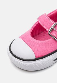 Zapatilla de lona rosa con un diseño cortado, puntera de goma blanca y una correa con hebilla metálica. Suela negra con textura estampada.