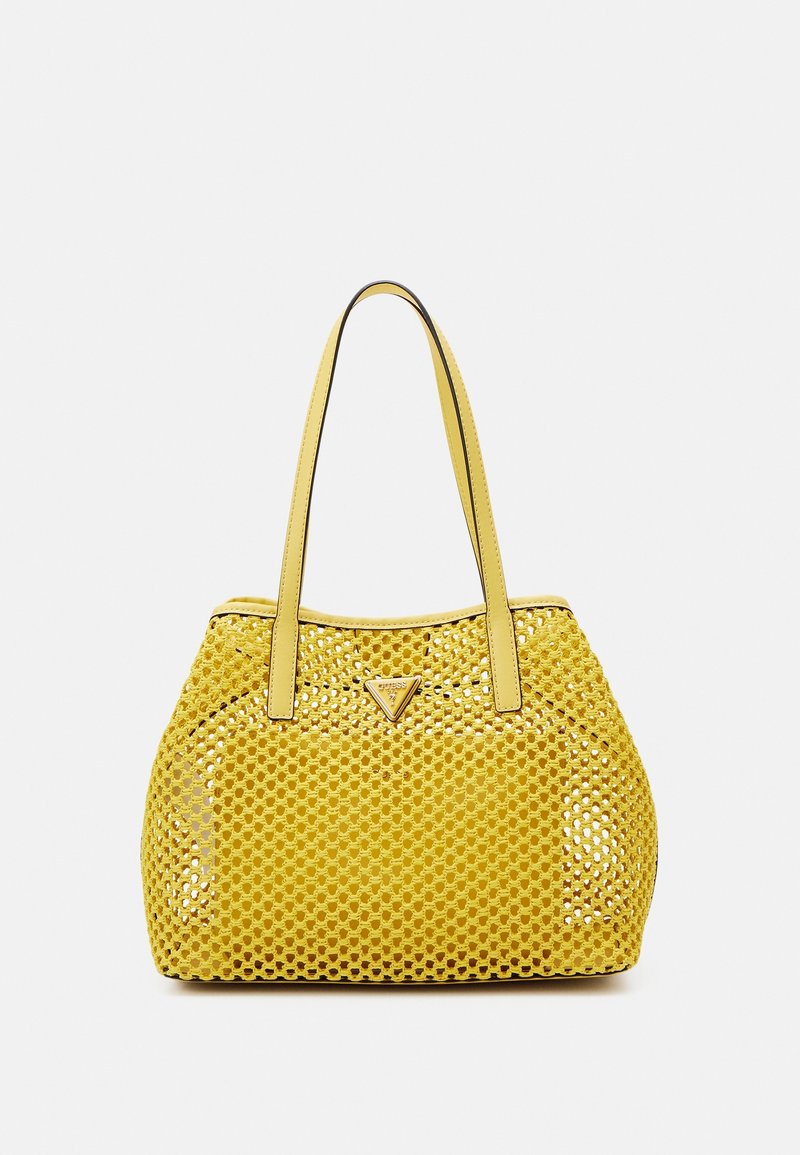 Sac fourre-tout en cuir jaune avec un motif perforé, deux poignées, et un détail de logo triangulaire à l'avant. Texture lisse, forme arrondie.