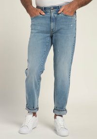 Jeans in denim azzurro chiaro con vestibilità rilassata, caratterizzati da dettagli strappati, orli arrotolati e tasche frontali. Abbinati a sneaker bianche.