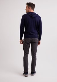Mörkblå hoodie i mjukt tyg, med snörning i huvan, ribbade ärmslut och smal passform. Stylingen kompletteras med grå slim-fit byxor och sneakers.