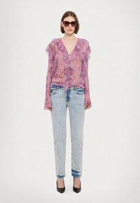 Caurskatīga violeta blūze ar volānu malām, kopā ar gaismati ziliem džinsiem un melniem augstpapēžu apaviem. Modelis valkā tumšas saulesbrilles.